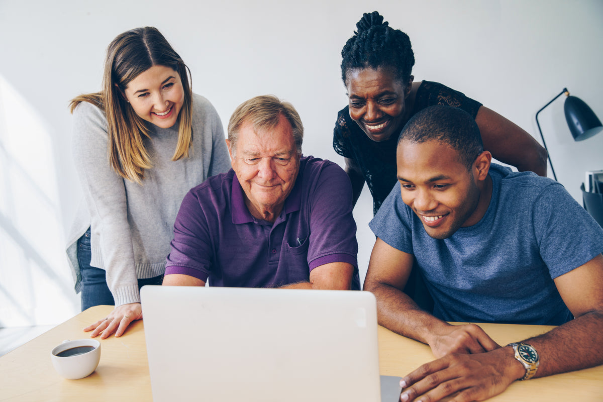 Colleagues gathered around a laptop, smiling at the screen