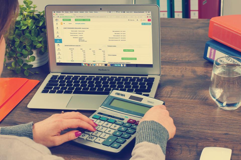 A person working through figures on a calculator beside a laptop spreadsheet