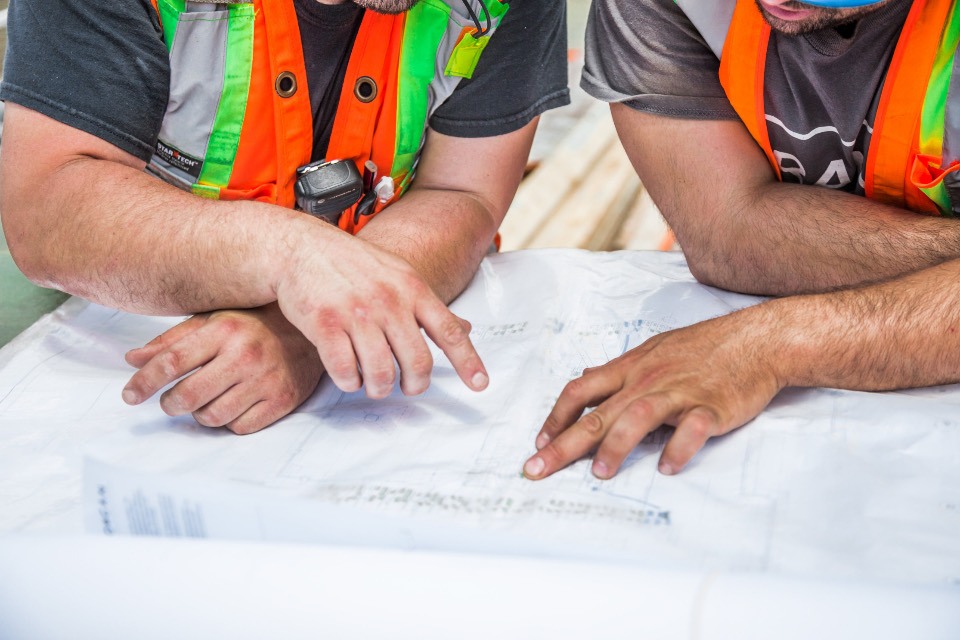 Two workers in high-visibility vests reviewing plans