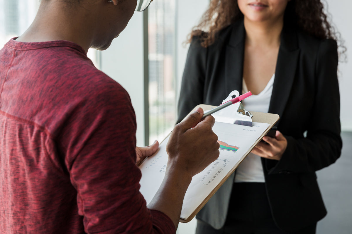 Two colleagues reviewing a document on a clipboard