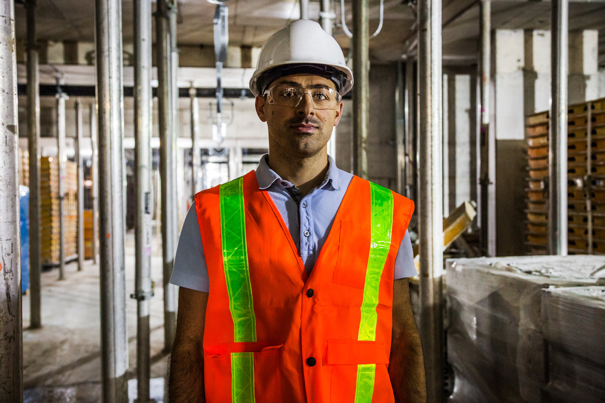 A warehouse worker in a hard hat and high-visibility vest between storage racks